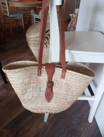 Pictured is a French Market tote bag with long leather handles, hung from the wrung of a chair by its handles.